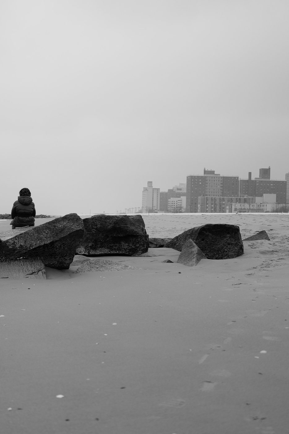 Personne assise sur les rochers face aux immeubles de Coney Island